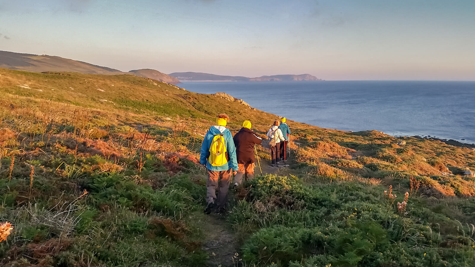 Marly Camino pilgrims walking a coastal trail at sunset